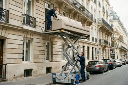 Deux déménageurs professionnels utilisant un monte-meuble pour descendre un grand canapé depuis un appartement haussmannien à Paris